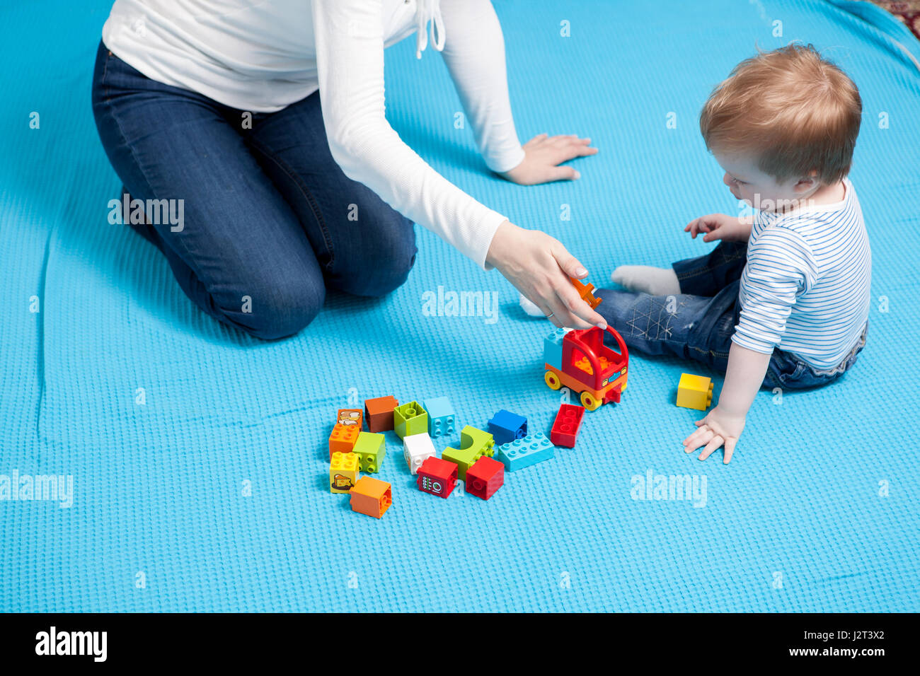 Preatty baby boy playing with toys on the floor next to her moth Stock