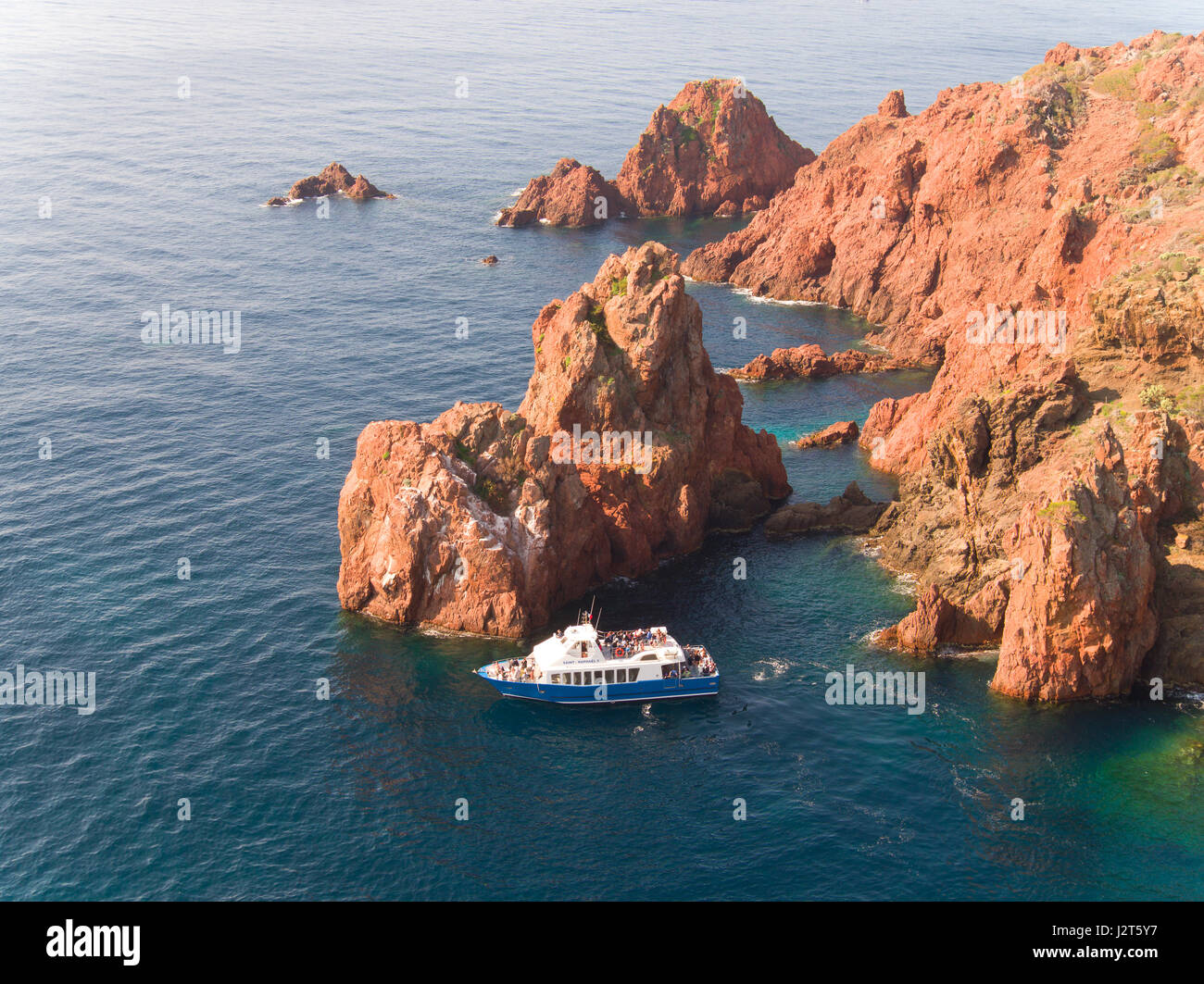 AERIAL VIEW. Tourists on a sightseeing boat admiring the spectacular red rock of Cap du Dramont. Saint-Raphël, Var, French Riviera, France. Stock Photo