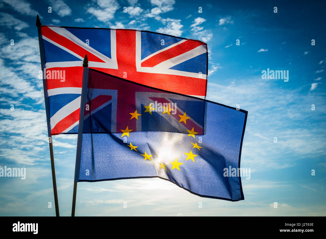 EU European Union and UK United Kingdom flags flying together in bright blue sky on the dawn of a new day of cooperation Stock Photo