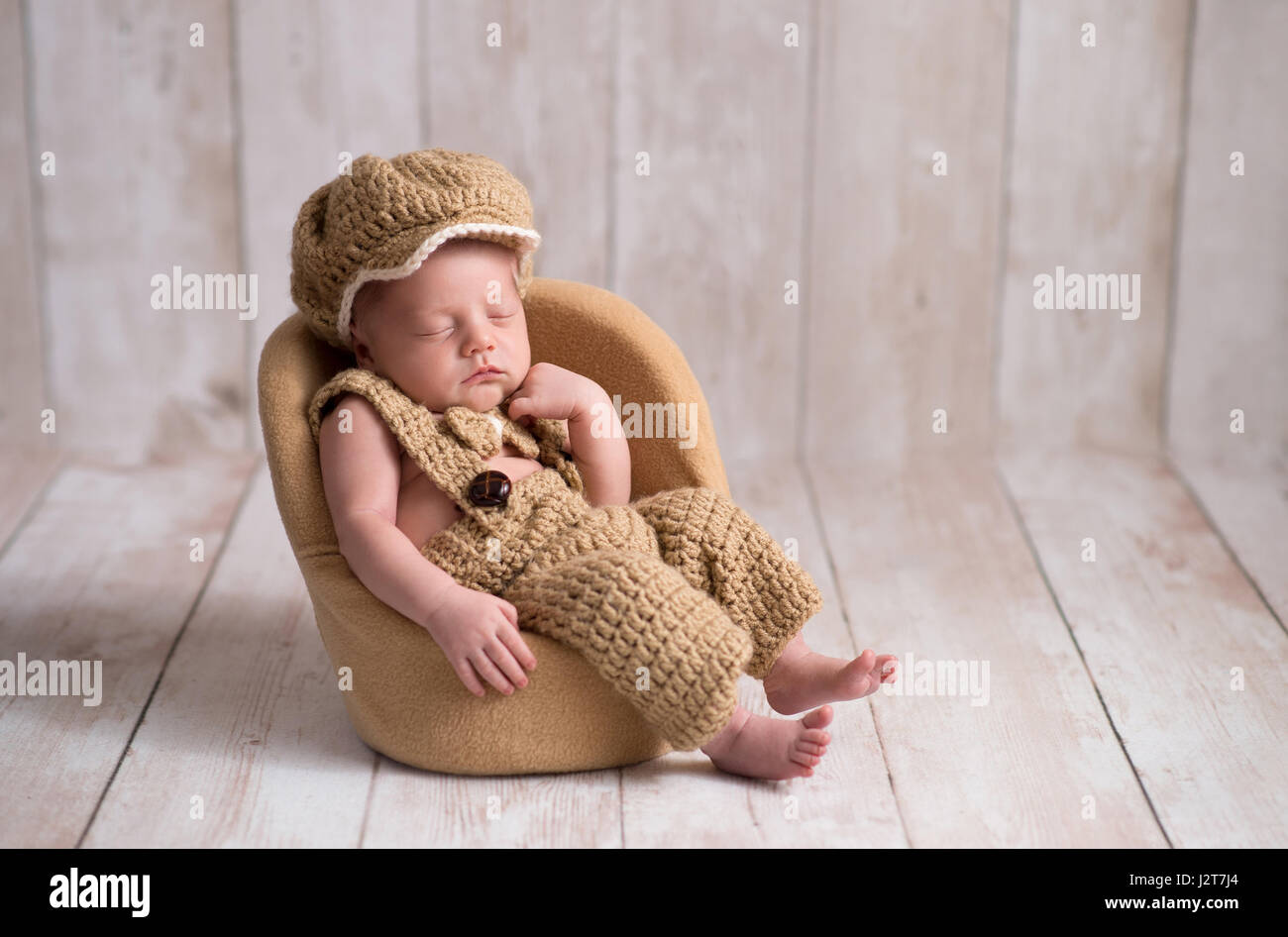 Nine day old, newborn baby boy wearing a crocheted, little man suit with newsboy cap and bowtie. He is sleeping in a tiny chair with a fist under his  Stock Photo