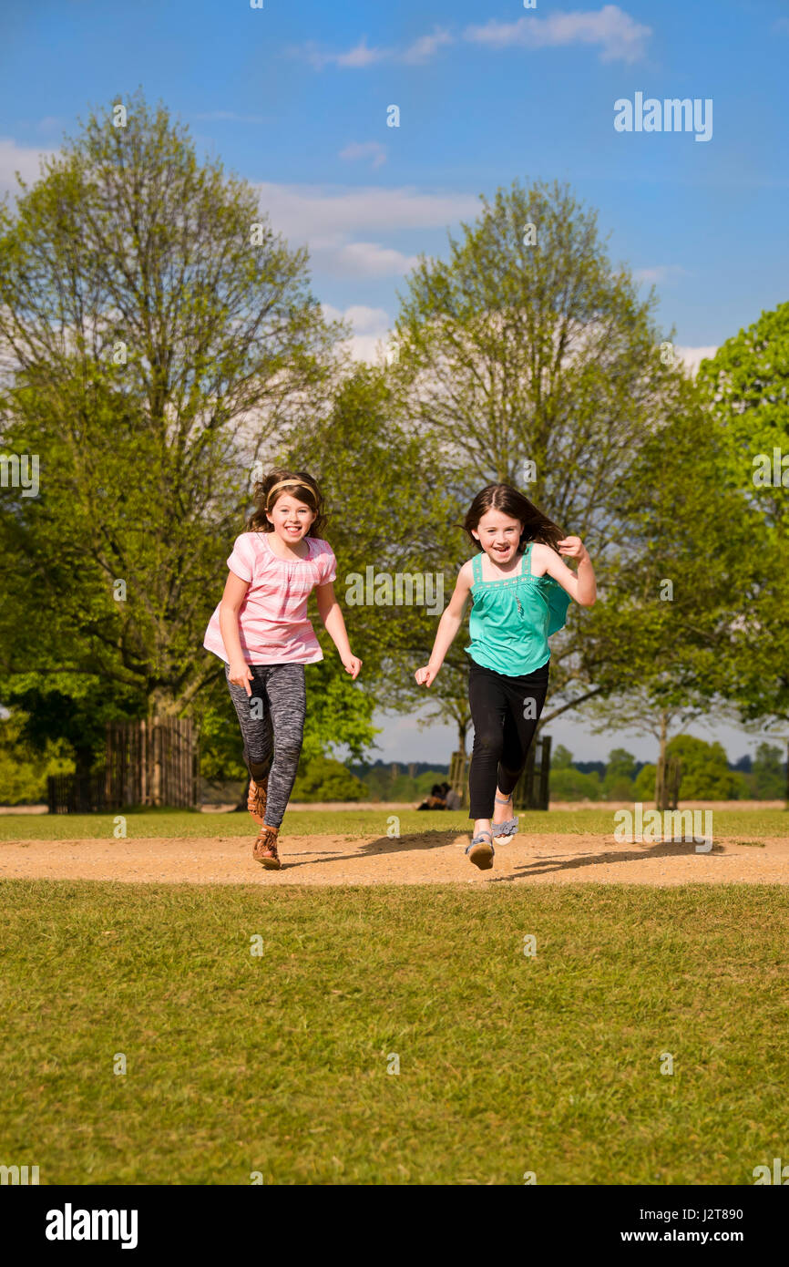 Vertical portrait of girls running across a park in the sun. Stock Photo