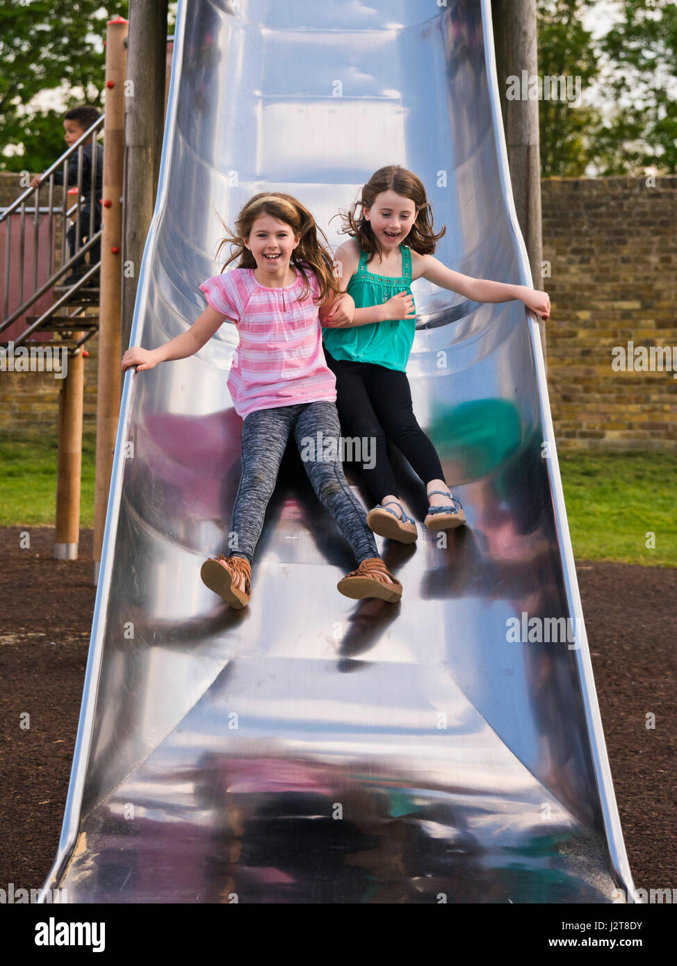 Vertical portrait of two girls sliding down a slide together in the