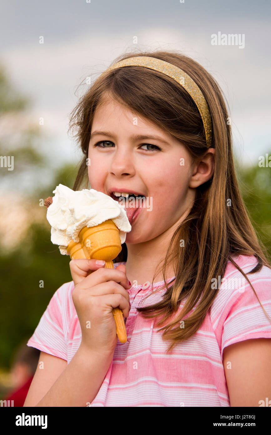 Vertical portrait of a young girl eating an ice cream in the sun. Stock Photo