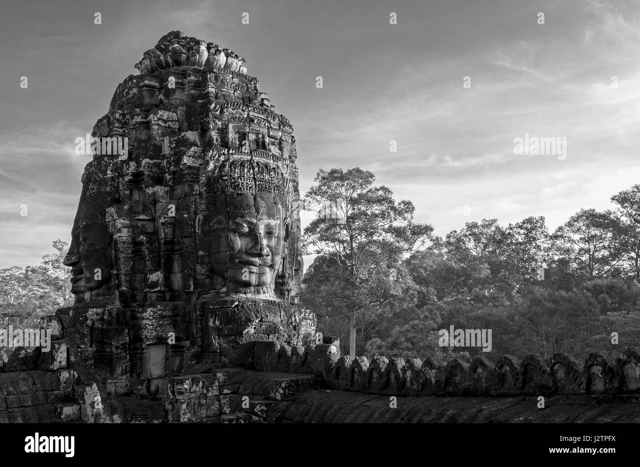 Black and white photograph of a smiling buddha head inside the bayon temple with the jungle in the background in angkor thom cambodia