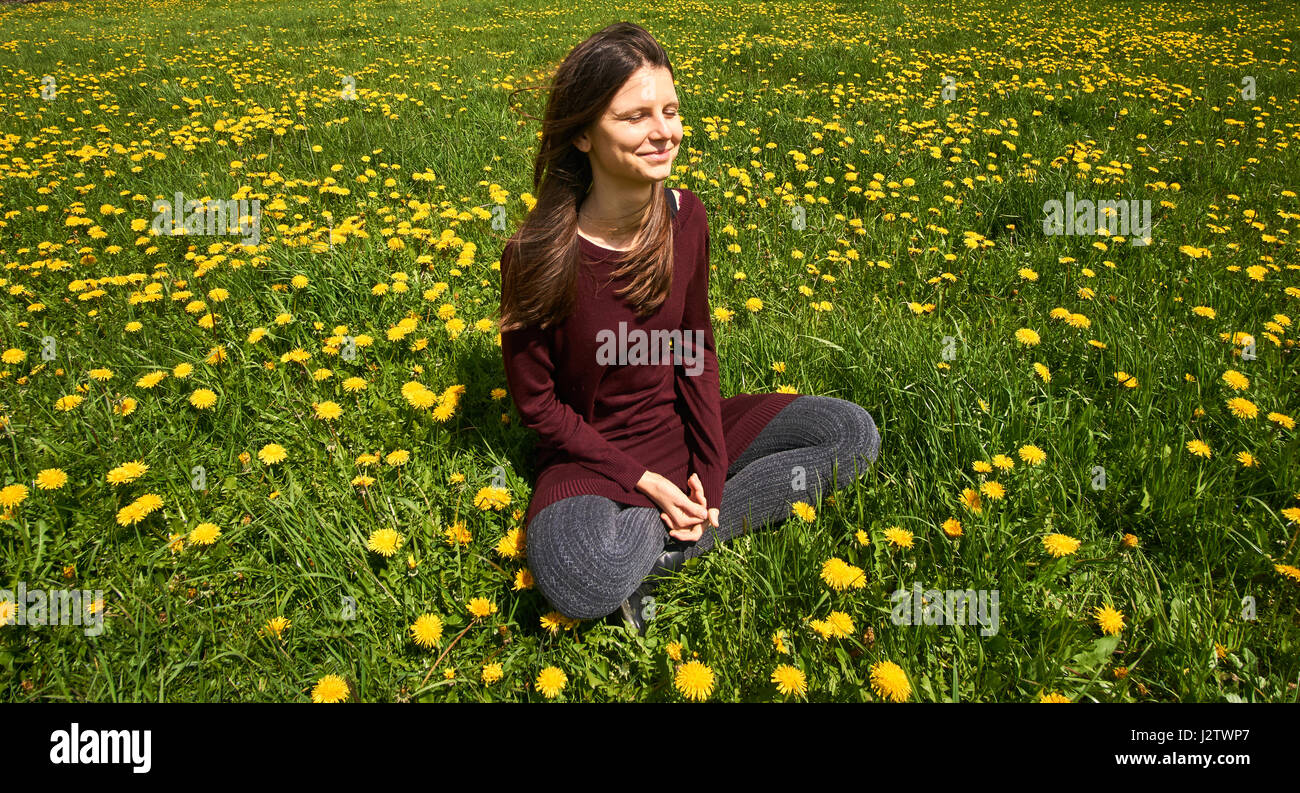 Beautiful young woman relaxing on a meadow with many dandelions in the spring sun. Smiling with copyspace. Stock Photo