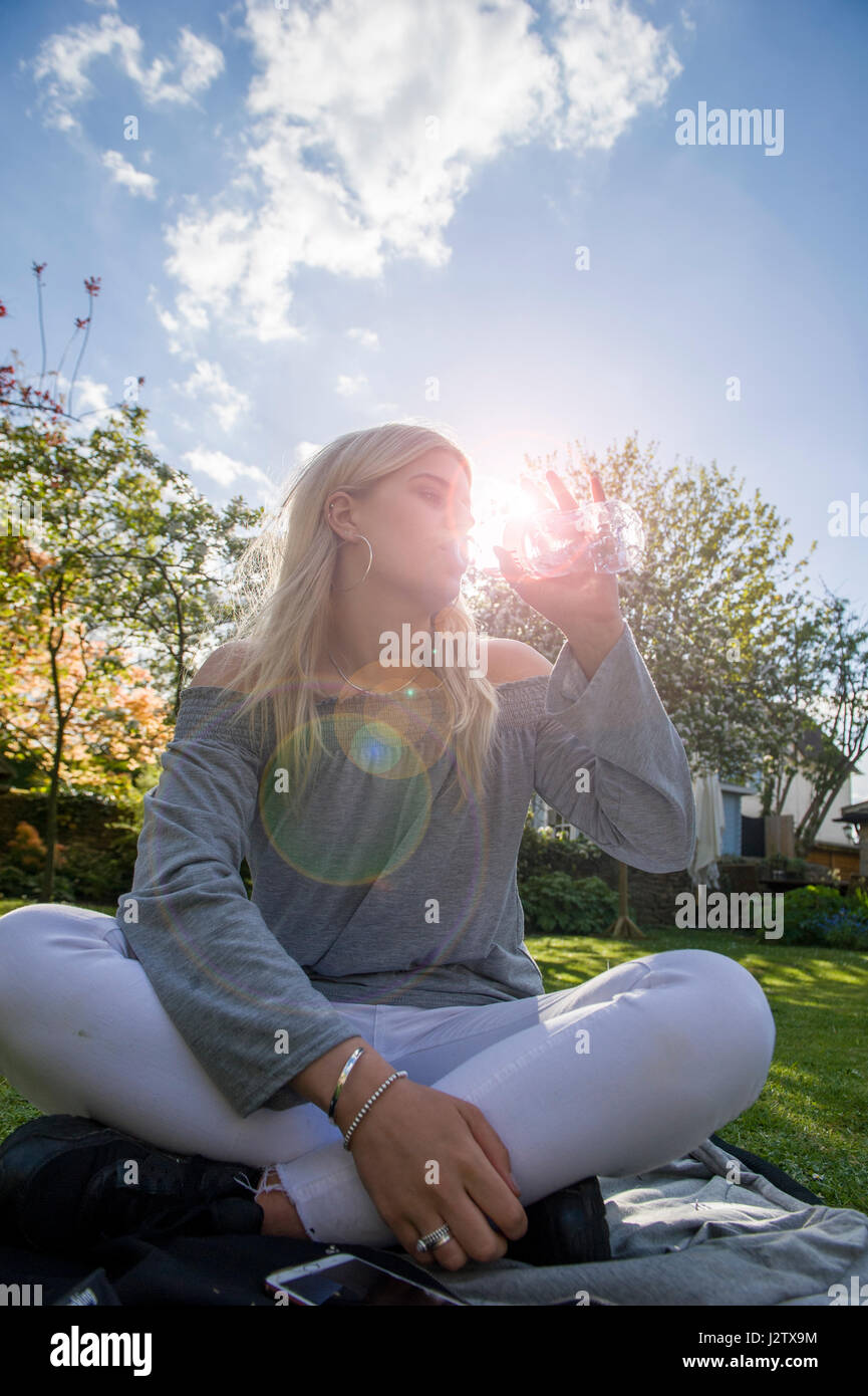 A beautiful girl enjoys a drink of water with the sunlight streaming ...