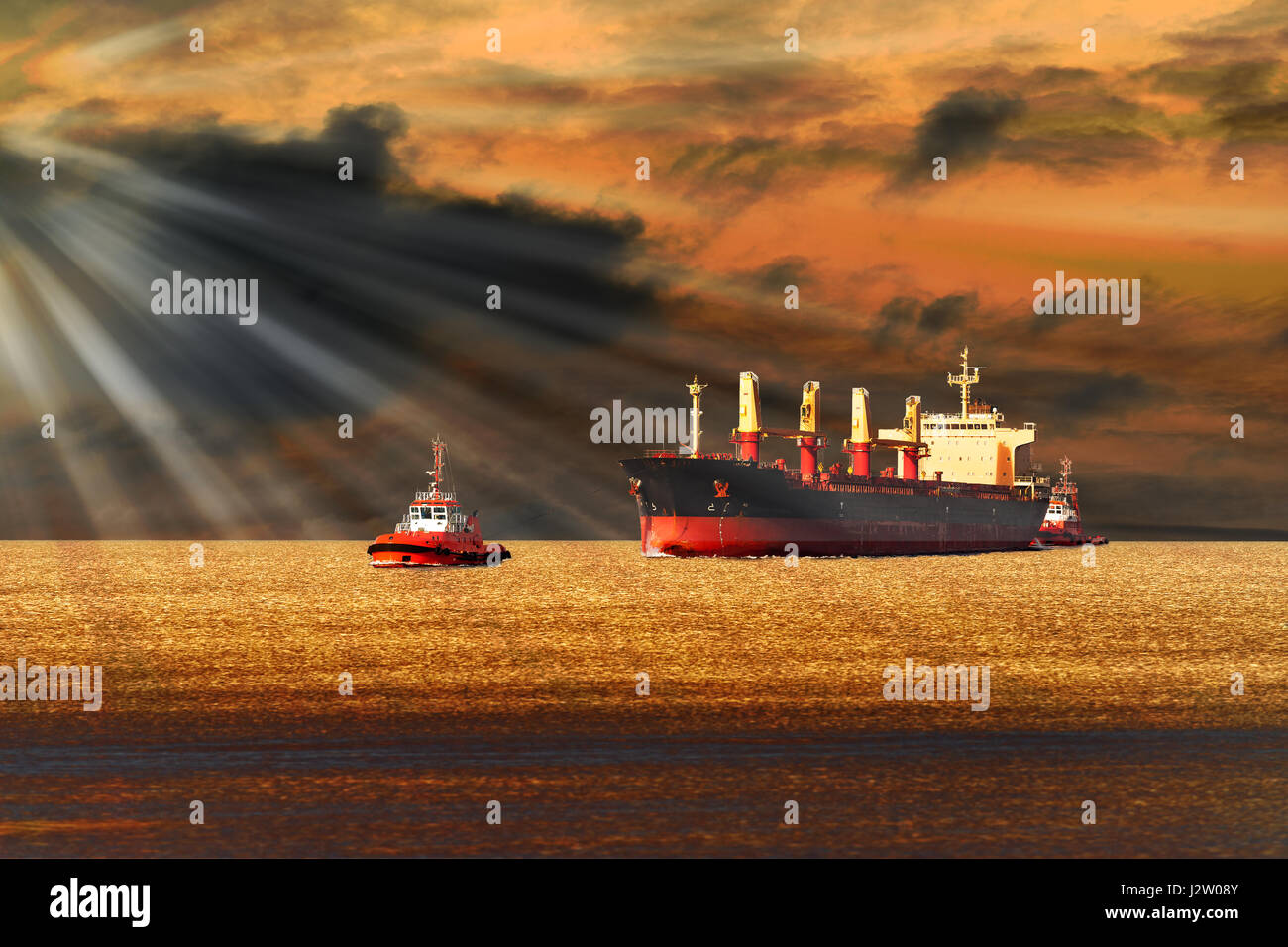 Tugboats towing a large cargo ship on sea. Stock Photo