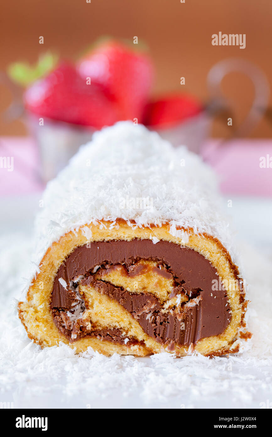 Chocolate coconut cake roll spreaded with coconut flour with strawberries in the background. Stock Photo