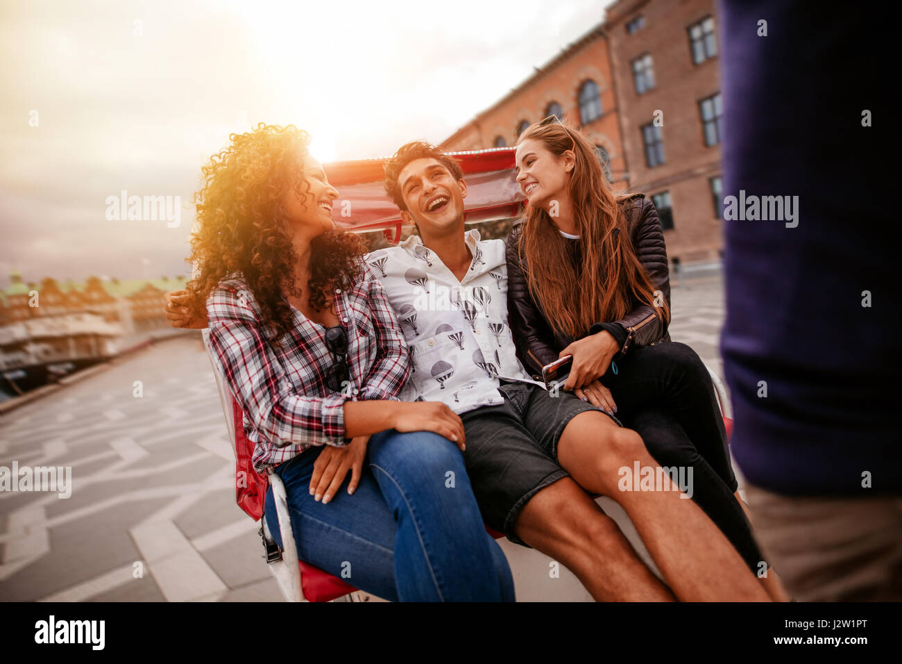 Cheerful teenage friends on tricycle. Young man and women riding on tricycle on road and having fun. Stock Photo