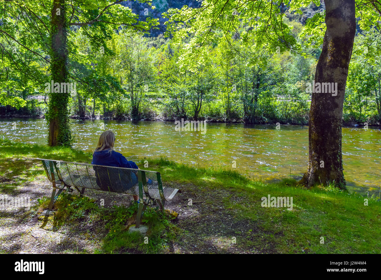 Back view of female figure sat on bench looking at lake river Stock Photo