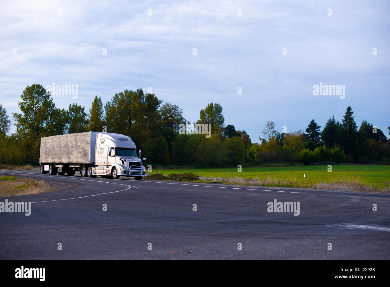 Excellent modern long haul silver big rig semi truck with a protective grille and a covered trailer to transport commercial cargo moves on a broad hig Stock Photo