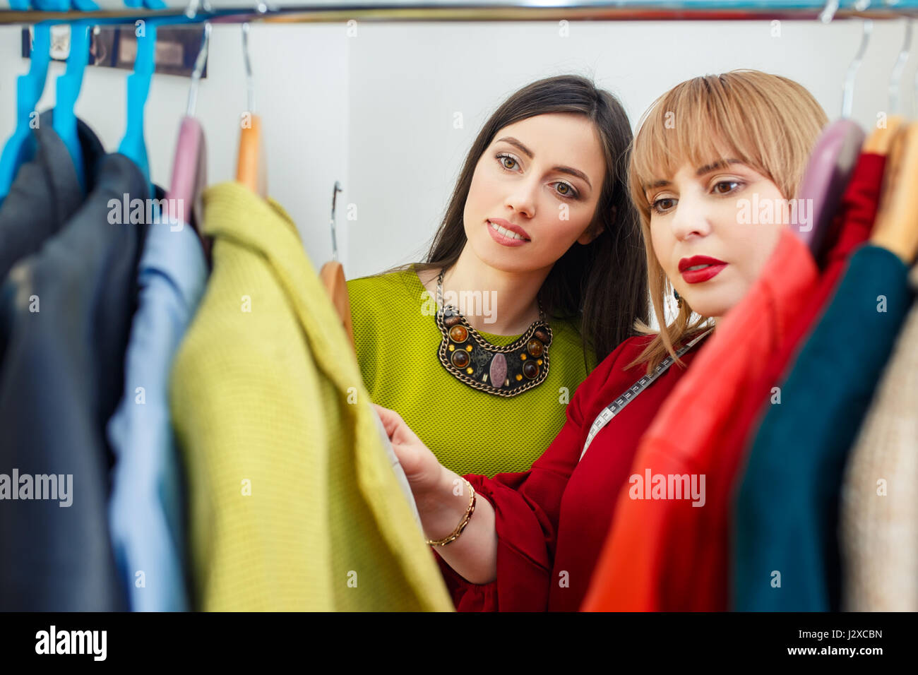 girl with stylist choosing her fashion outfit. Women looking at clothes hanging deciding what to wear. Analysis of wardrobe. Fashion stylist consultat Stock Photo