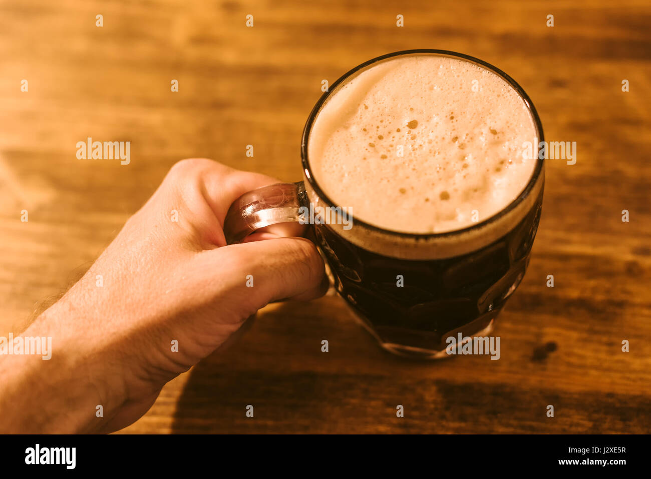Man drinking dark beer in british dimpled glass pint mug on bar table Stock Photo