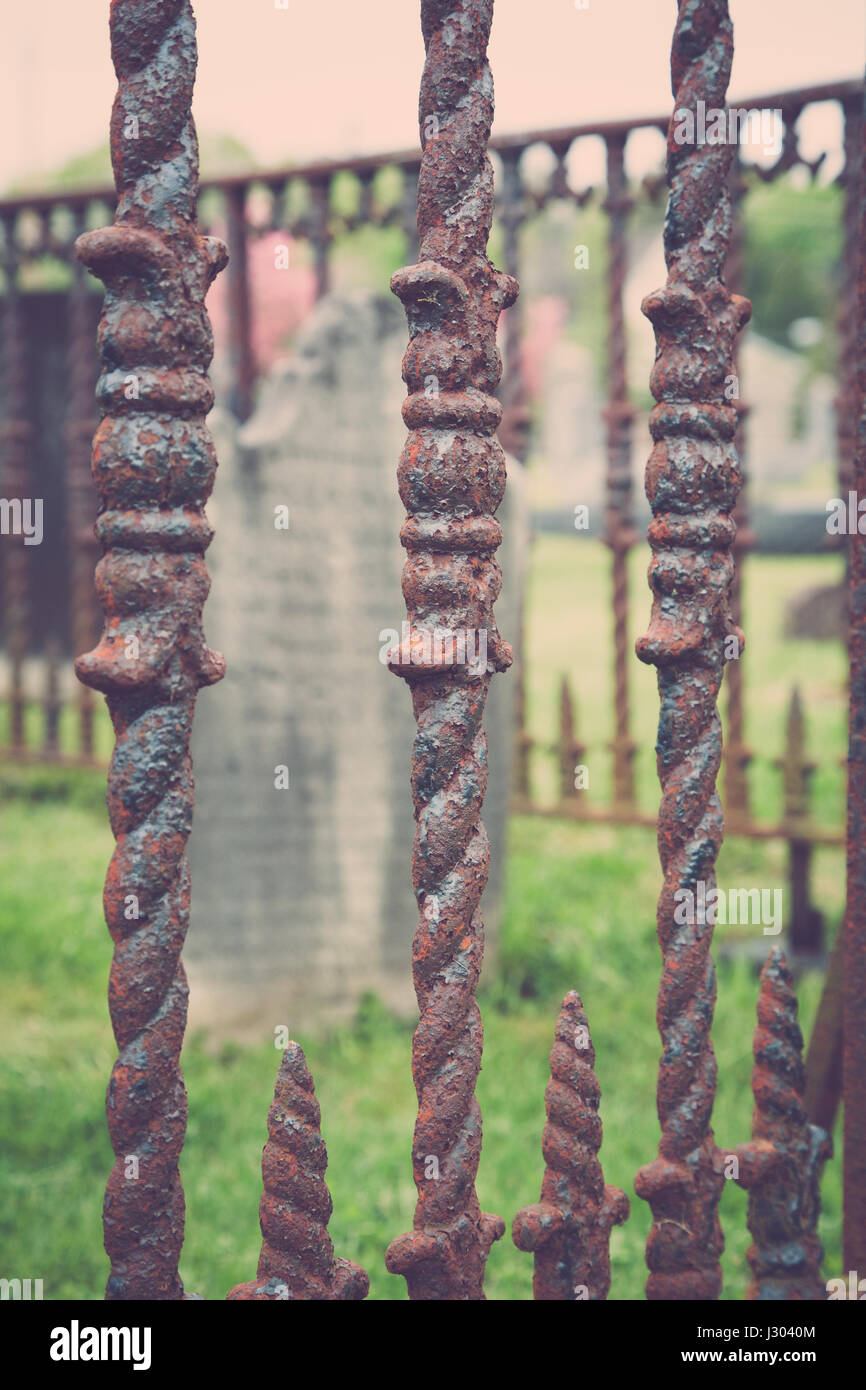 An old tombstone sits behind a rusty iron fence in a cemetery. Stock Photo