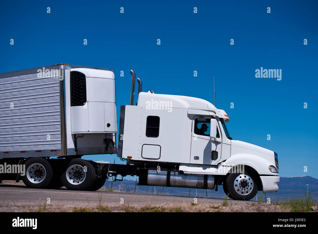 Big white truck with a trailer and a refrigeration unit on the road of the highway against the