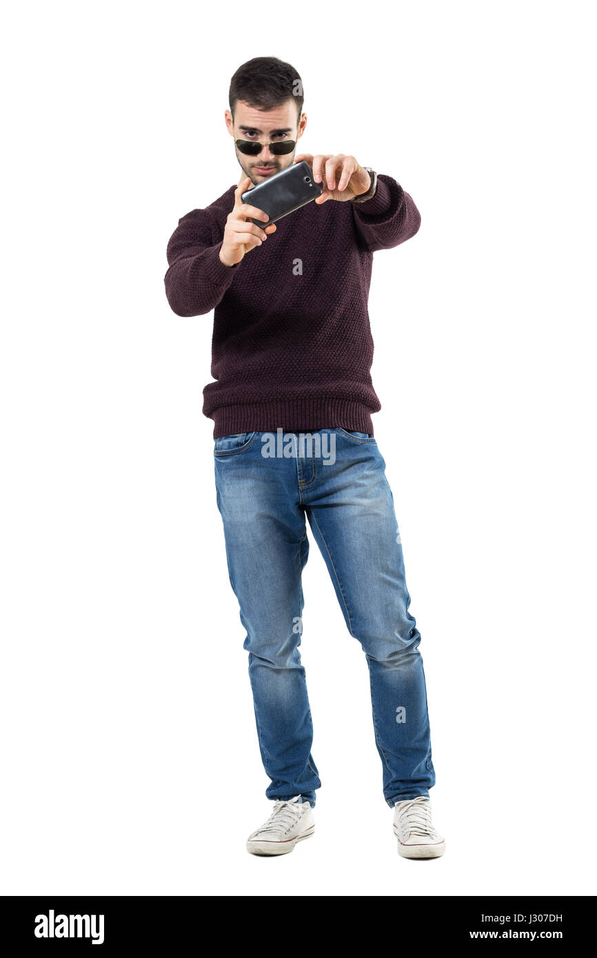 Concentrated young casual man taking picture with mobile phone. Full body length portrait isolated over white studio background. Stock Photo