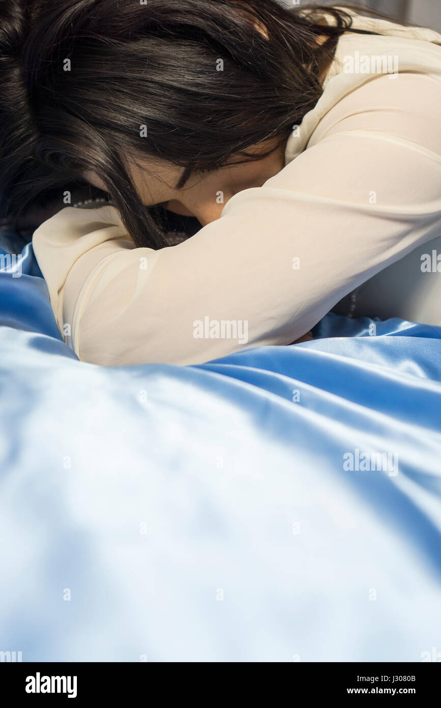 Sad young woman laying down in bed crying Stock Photo