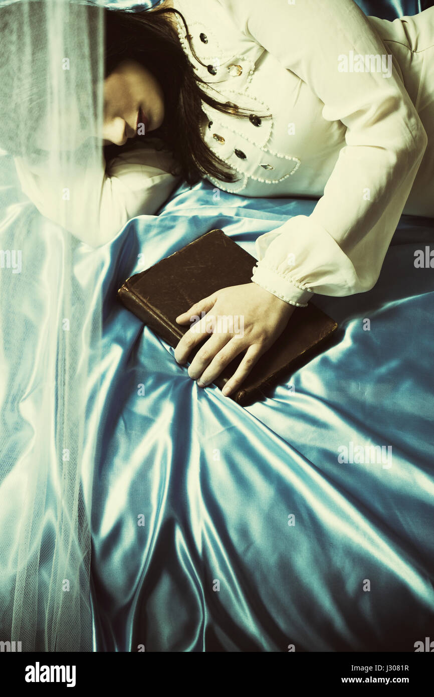 Sad young woman laying down in bed hand on book Stock Photo