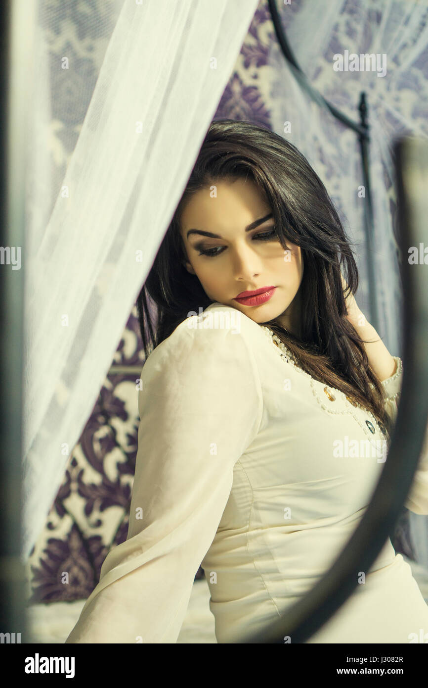 Beautiful young woman sat on bed looking away Stock Photo