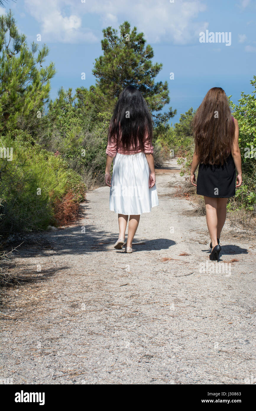 Rear view of two young women walking away together on a countryside road Stock Photo