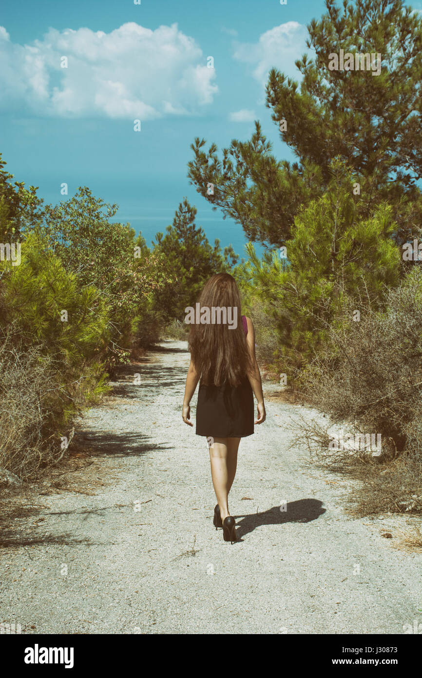 Full length rear view of a young woman walking away on a countryside road Stock Photo