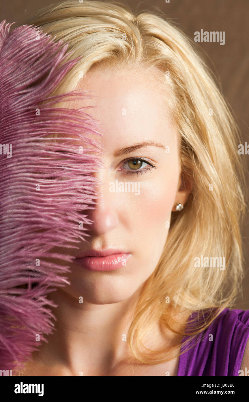 Beautiful blond woman hiding face with a pink feather Stock Photo