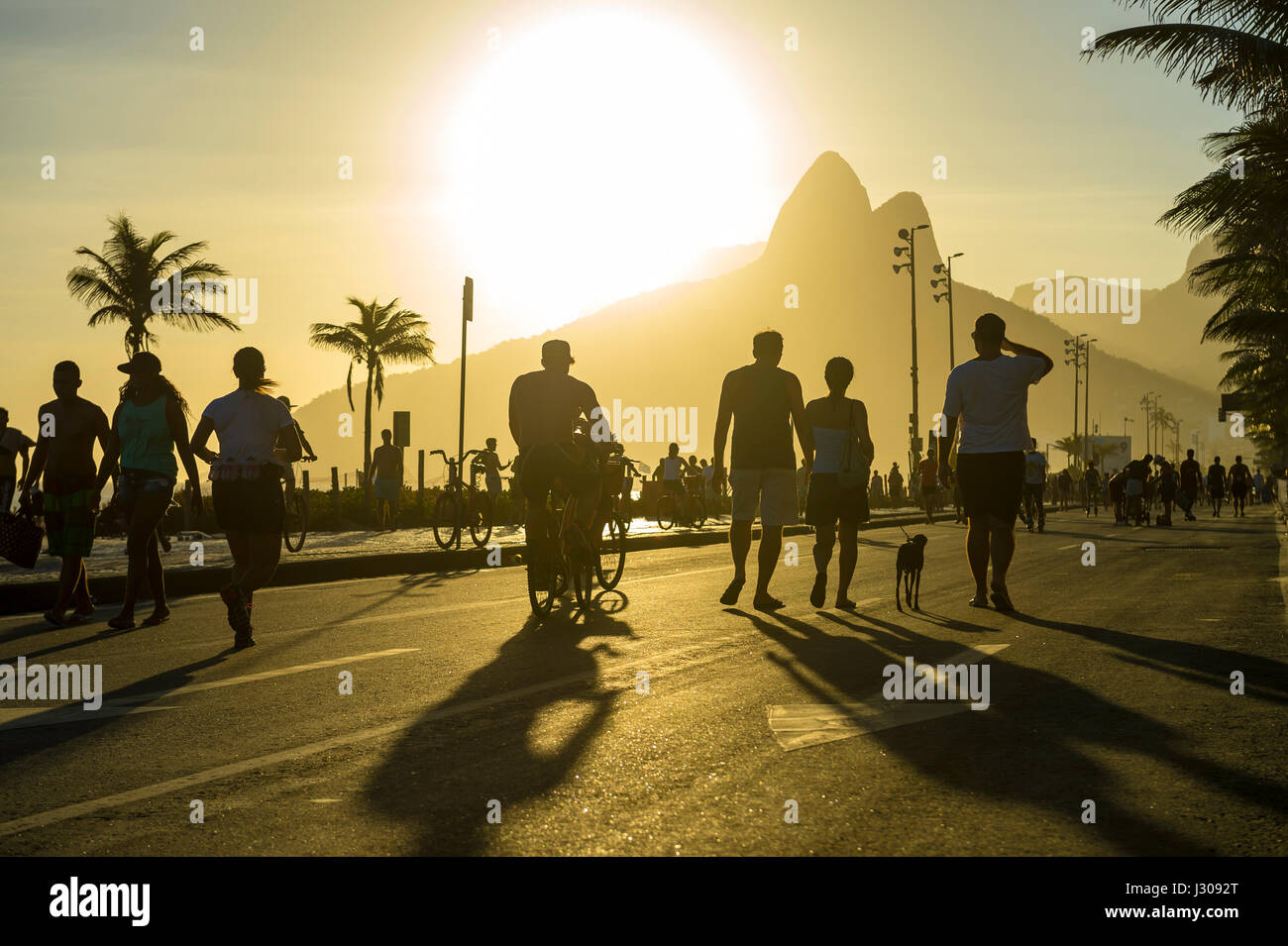 RIO DE JANEIRO - FEBRUARY 12, 2017: Silhouettes of Brazilians stroll along the beachfront Avenida Vieira Souto street in Ipanema at sunset. Stock Photo