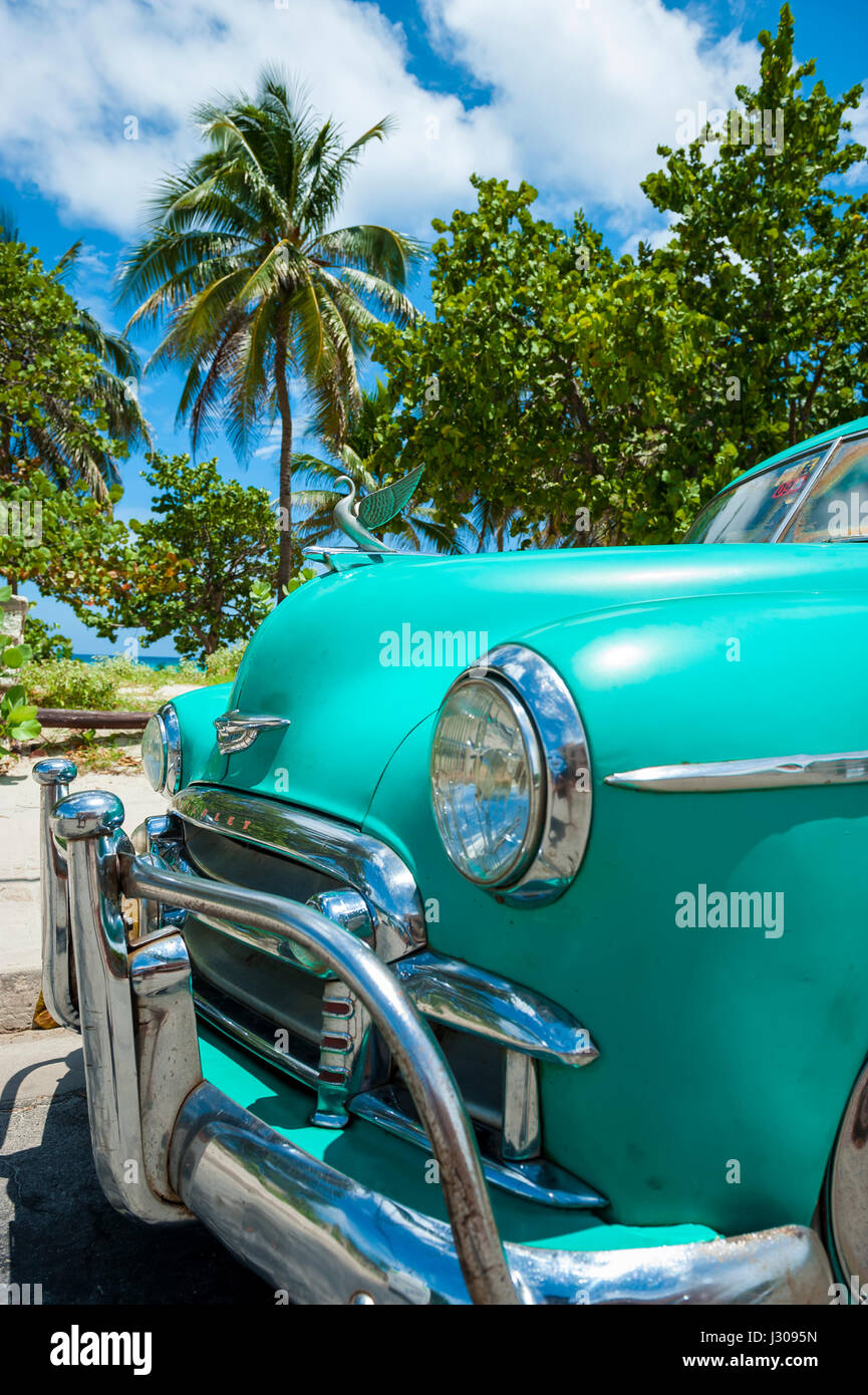 VARADERO, CUBA - JUNE, 2011: Bright colored vintage American car serving as a taxi stands parked next to the Caribbean beachfront. Stock Photo