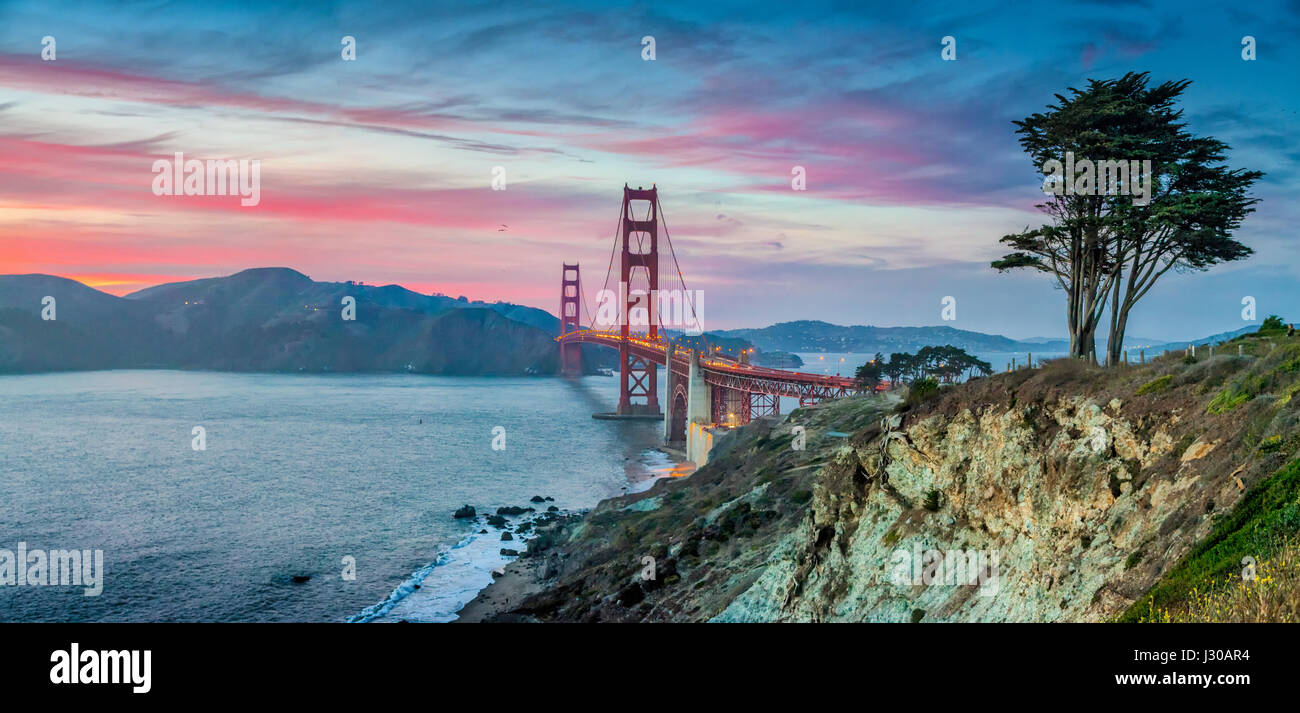 Classic panorama view of famous Golden Gate Bridge seen from scenic Baker Beach in beautiful post sunset twilight with blue sky and clouds at dusk Stock Photo