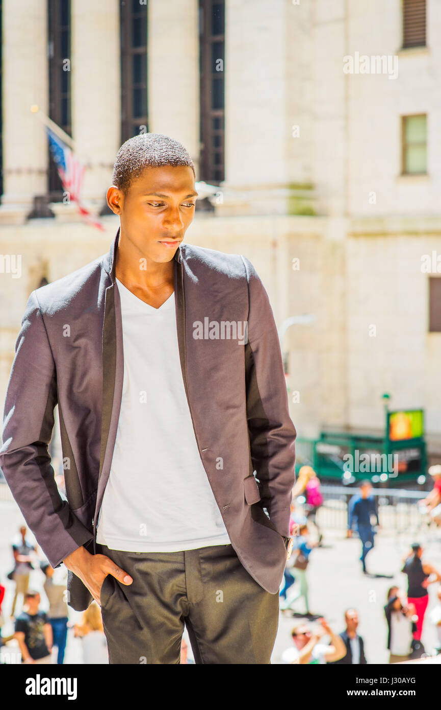 Unhappy Teenage Boy. Wearing a white under wear, fashionable jacket, a young black college student is standing outside office building, looking down,  Stock Photo