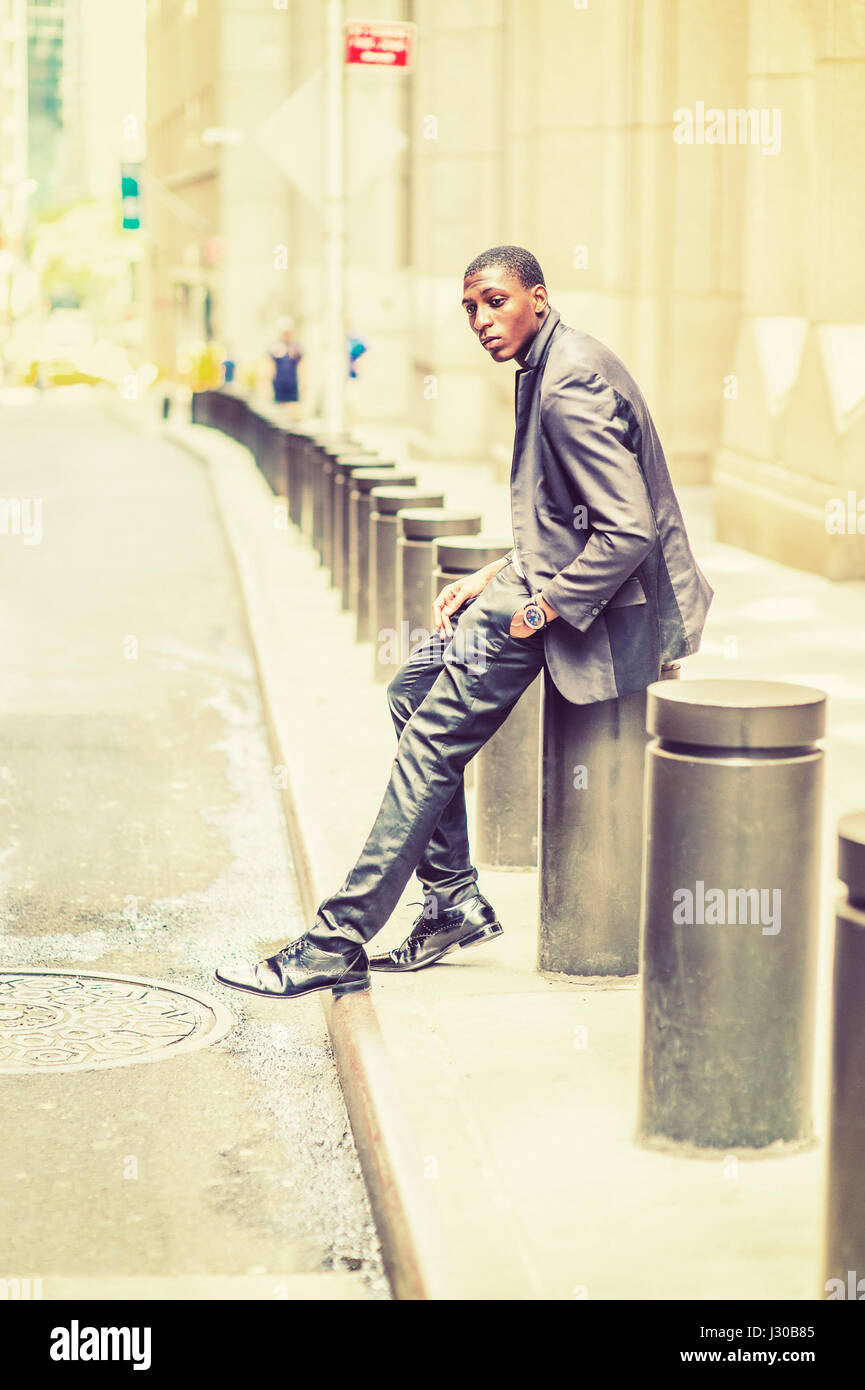 Young black teenage boy is sitting on street, hunchbacked, sad, tired, looking down, thinking, lost in thought. Man relaxing on street. Retro filtered Stock Photo