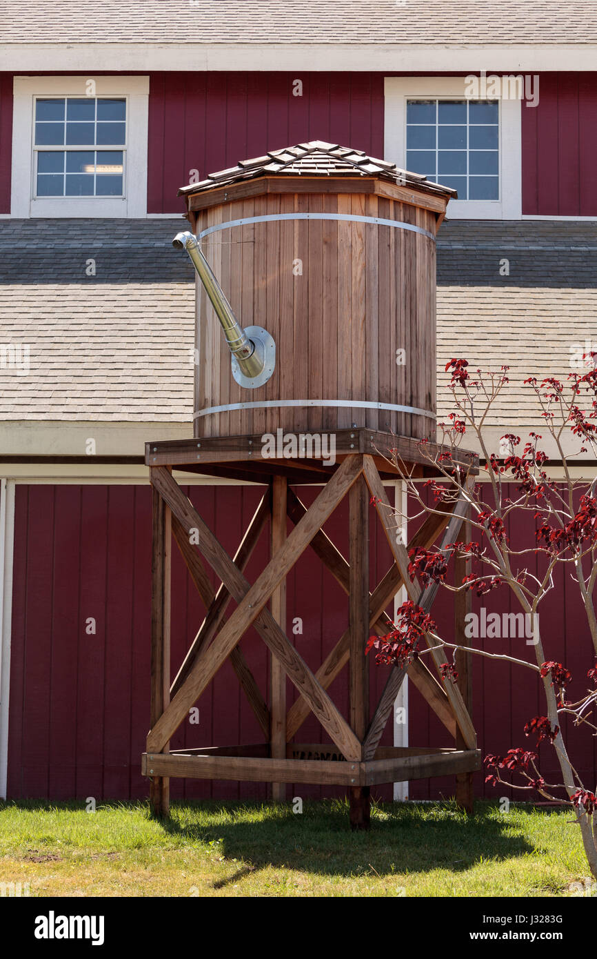Well water tower tank on a farm in summer with a maple tree and a barn ...