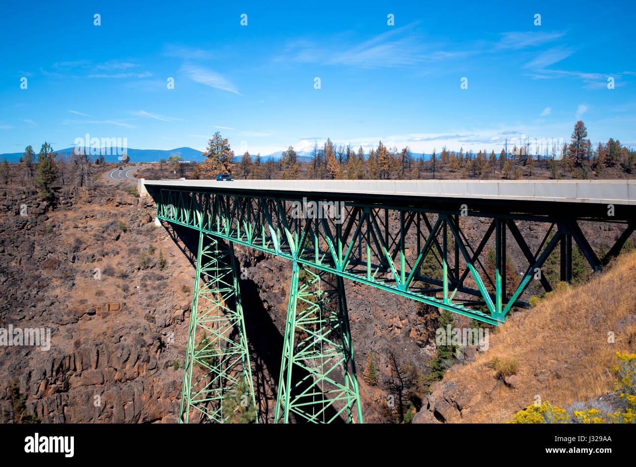 Green metal truss road bridge on two conical truss supports poles