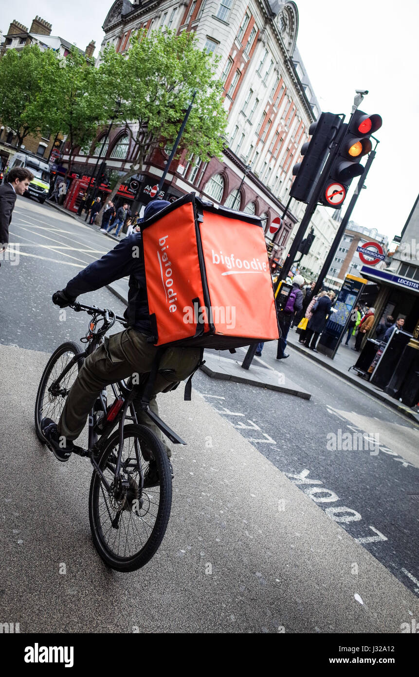 A Bigfoodie bike food delivery courier rushes through traffic in Central London. Bigfoodie compete with Deliveroo and Uber Eats Stock Photo