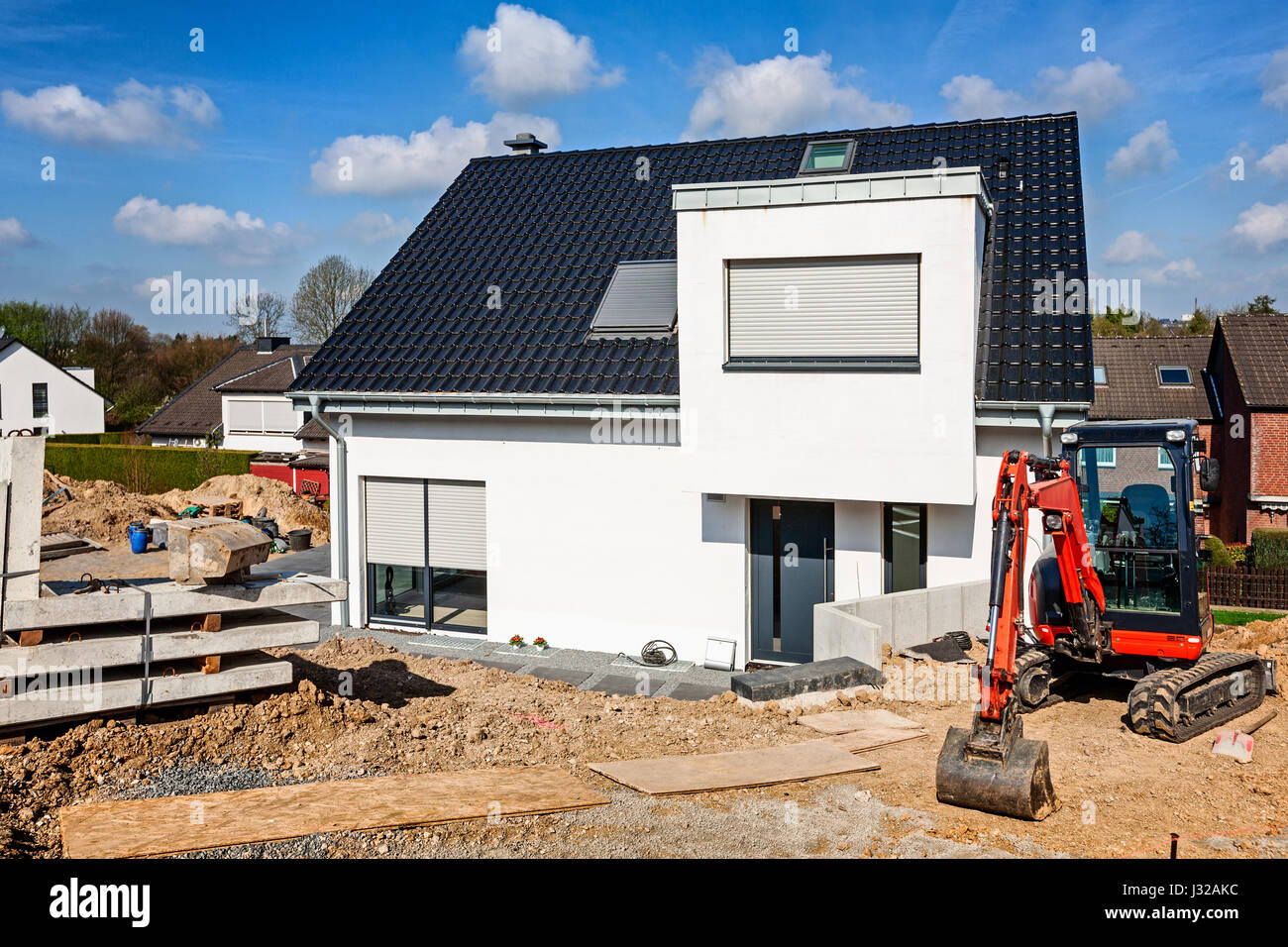 New white single family home and mini excavator, construction site near completion Stock Photo