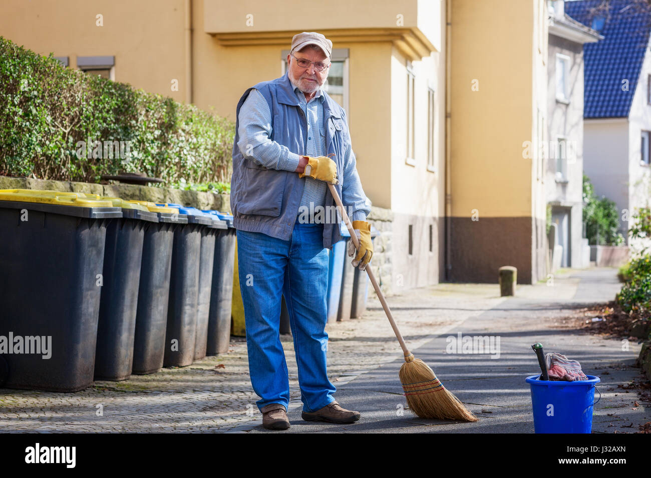 Elderly senior man with broom sweeping sidewalk on sunny day Stock Photo