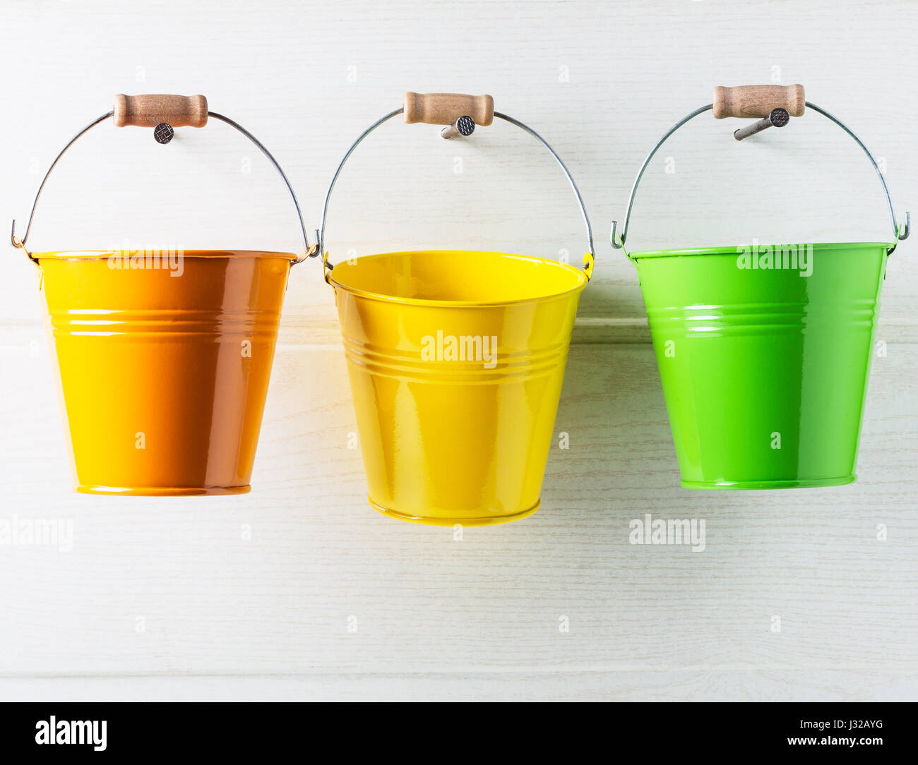 Bucket list concept. Three colorful buckets hanging on white wooden wall Stock Photo