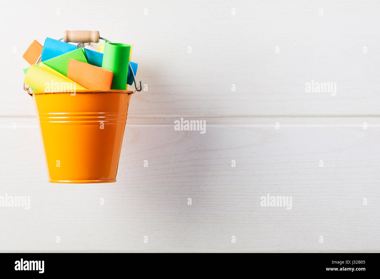 Bucket list concept. Orange bucket with colorful paper notes hanging on white wooden wall Stock Photo