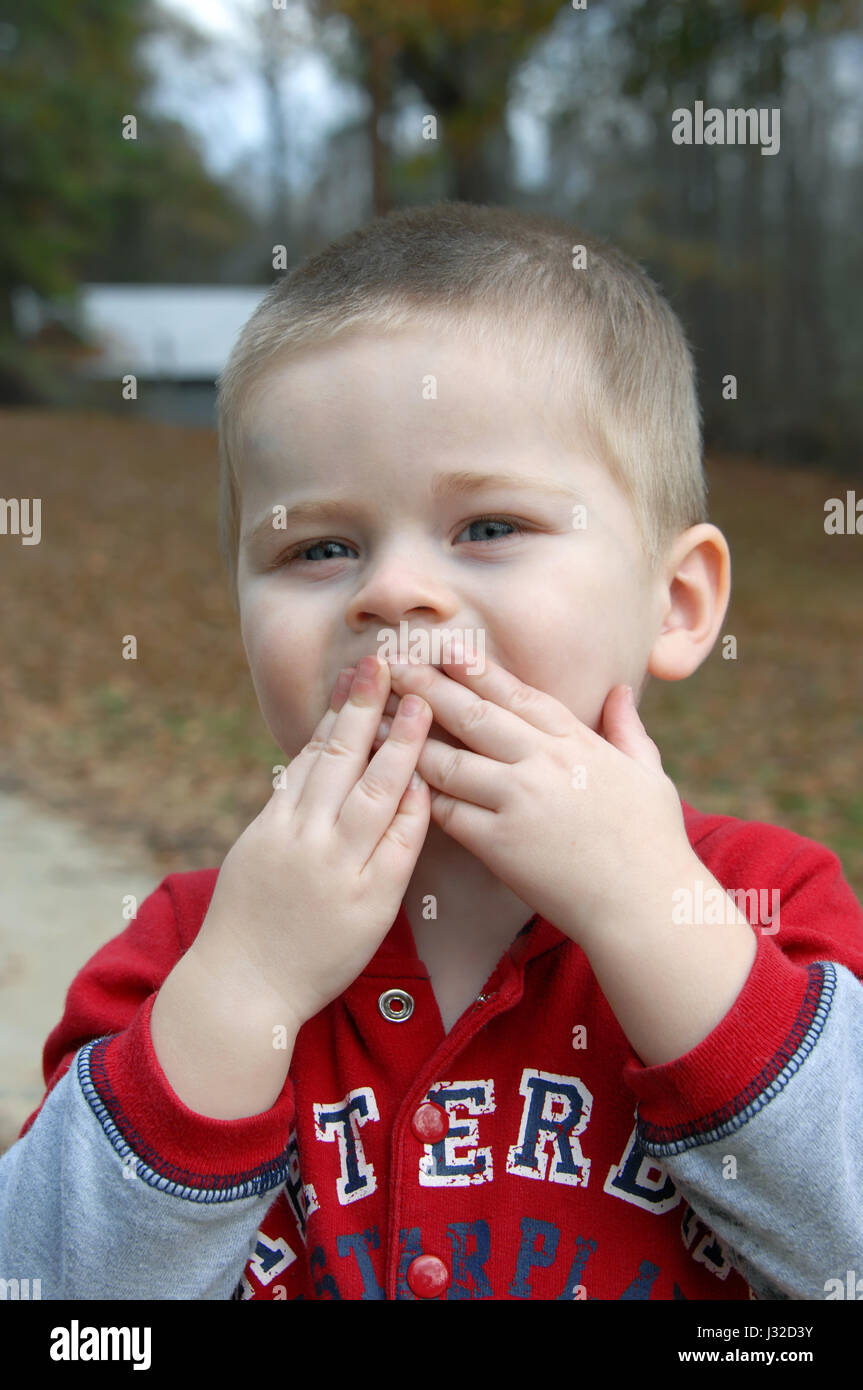 Little boy covers his mouth with both hands to "blow a kiss". He has