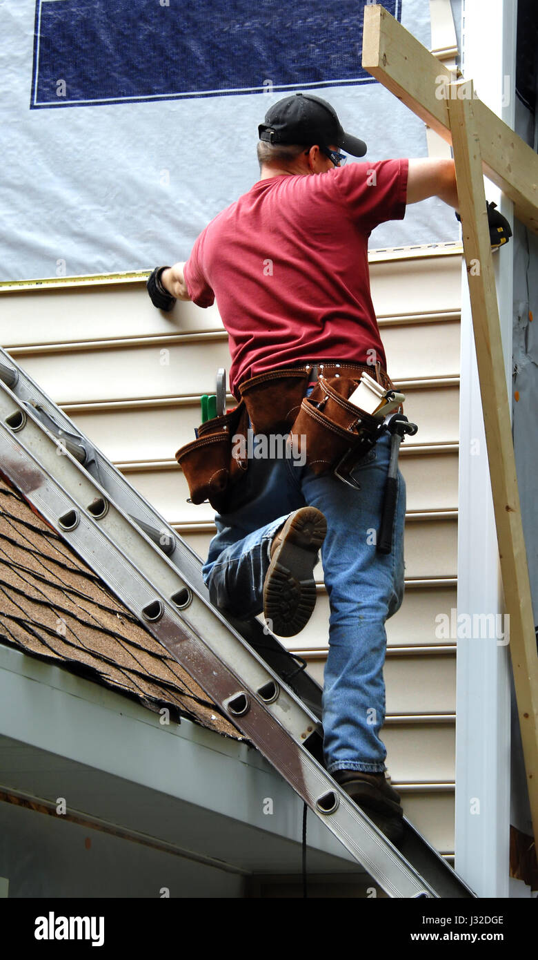 Young home owner remodels his older home by installing siding.  This do-it-yourselfer is measuring for the next sheet to be installed. Stock Photo
