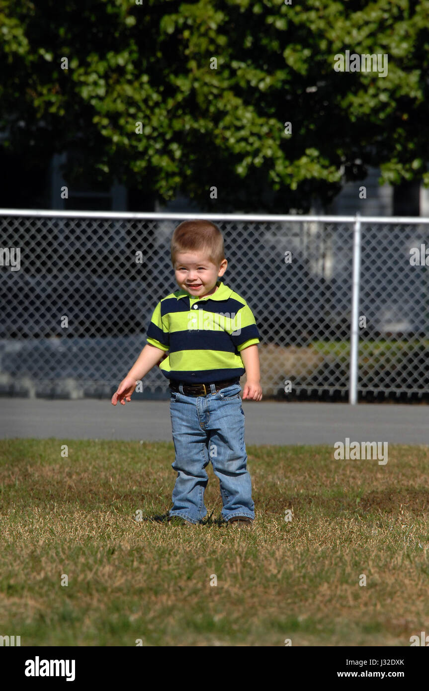 Full length image of little boy in polo style shirt, tucked into denim jeans.  Little boy is smiling and squinting because of the bright sunshine. He  Stock Photo - Alamy