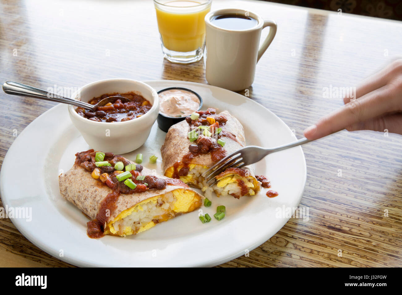 Breakfast burrito with salsa on a white diner plate with orange juice and coffee, on a wood