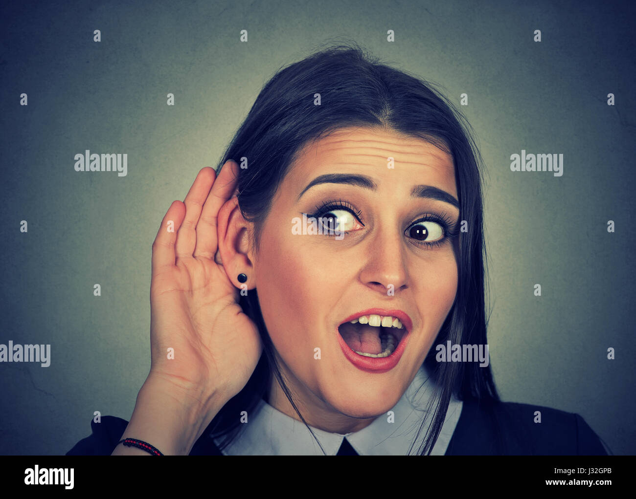 Surprised woman with hand to ear carefully secretly listening to gossip conversation isolated on gray background Stock Photo
