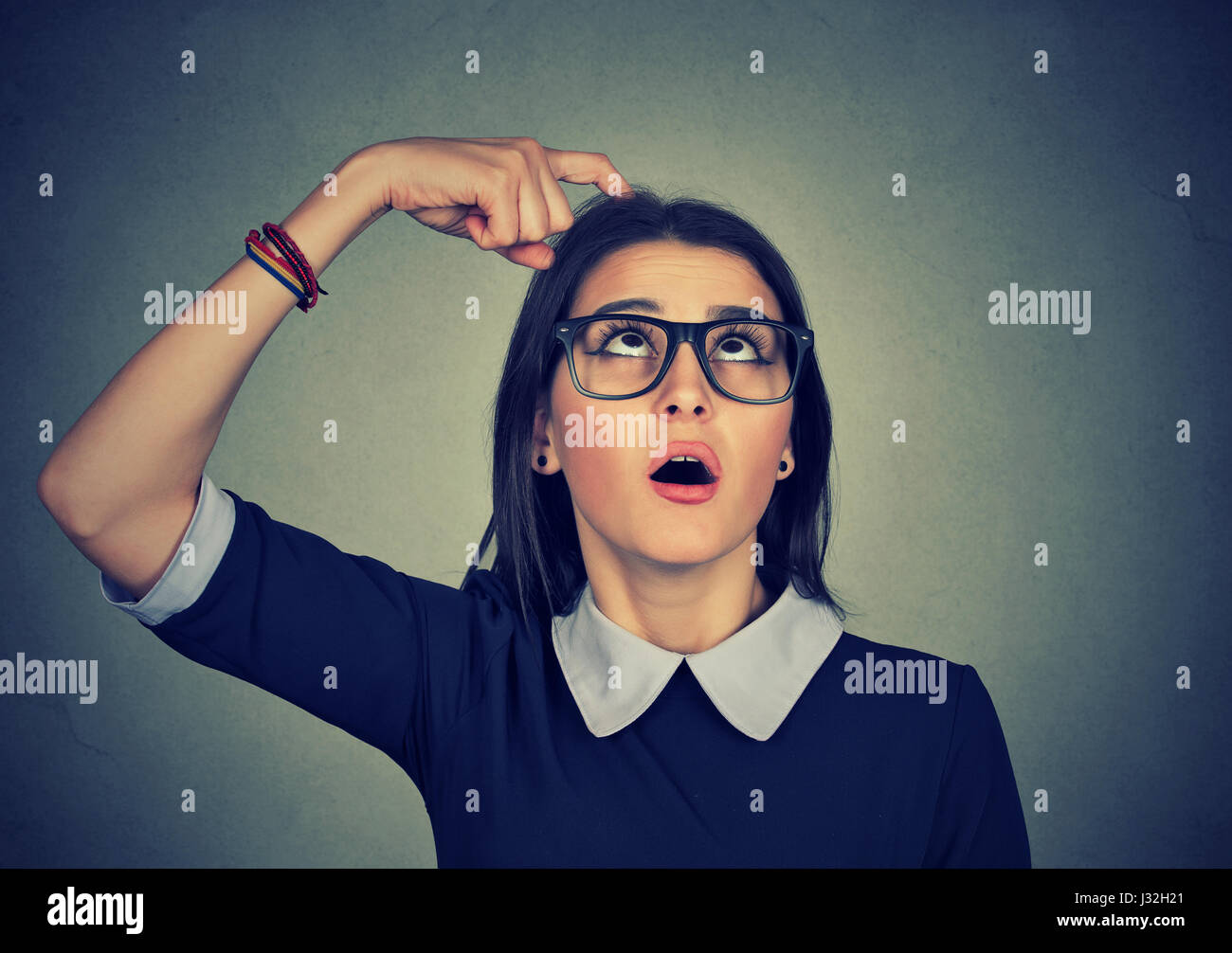 Closeup portrait young woman scratching head thinking about something looking up trying to recall isolated on grey wall background. Human facial expre Stock Photo