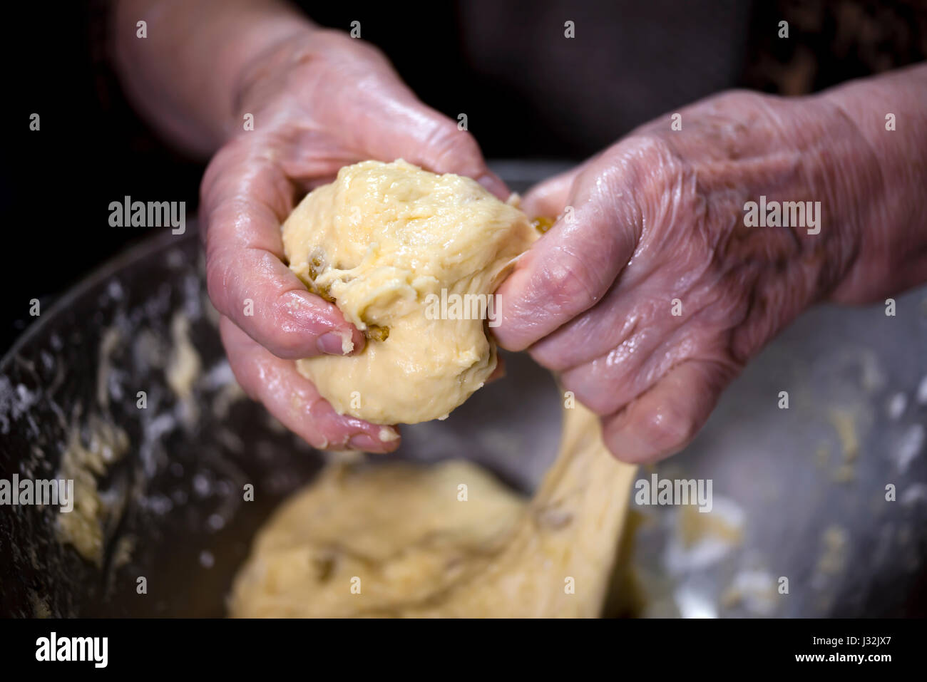 Butter oily dough is mixed with raisins in a large bowl wrinkled by