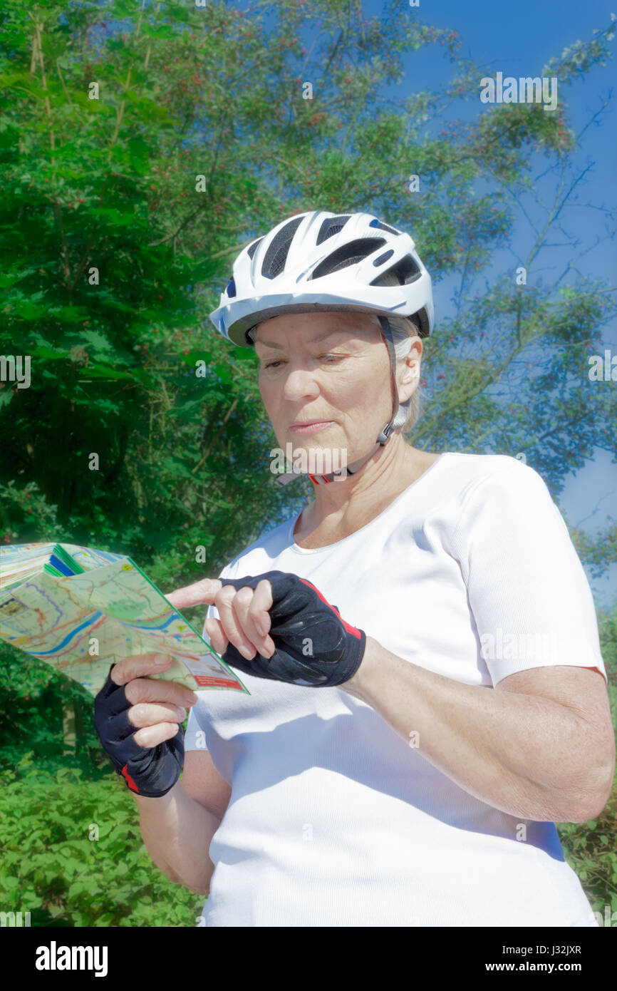 Senior woman outdoors in the summer sun with bicycle helmet, gloves, white t-shirt and map, getting a nice suntan and sufficient vitamin d Stock Photo