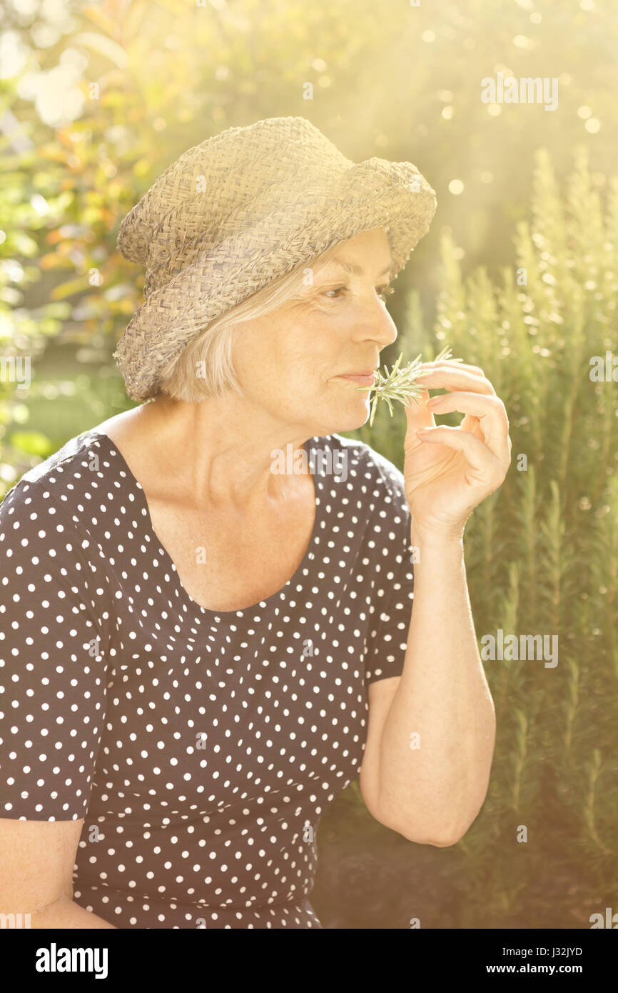 Senior woman in polka-dotted dress and straw hat sitting in her garden ...