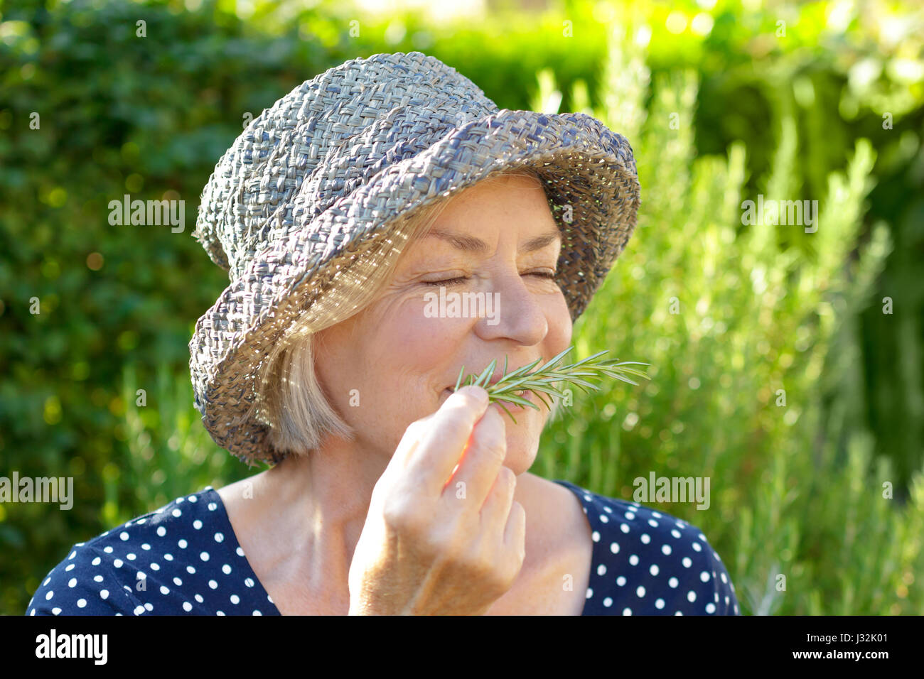 Senior woman with straw hat on a sunny summer afternoon in her garden ...