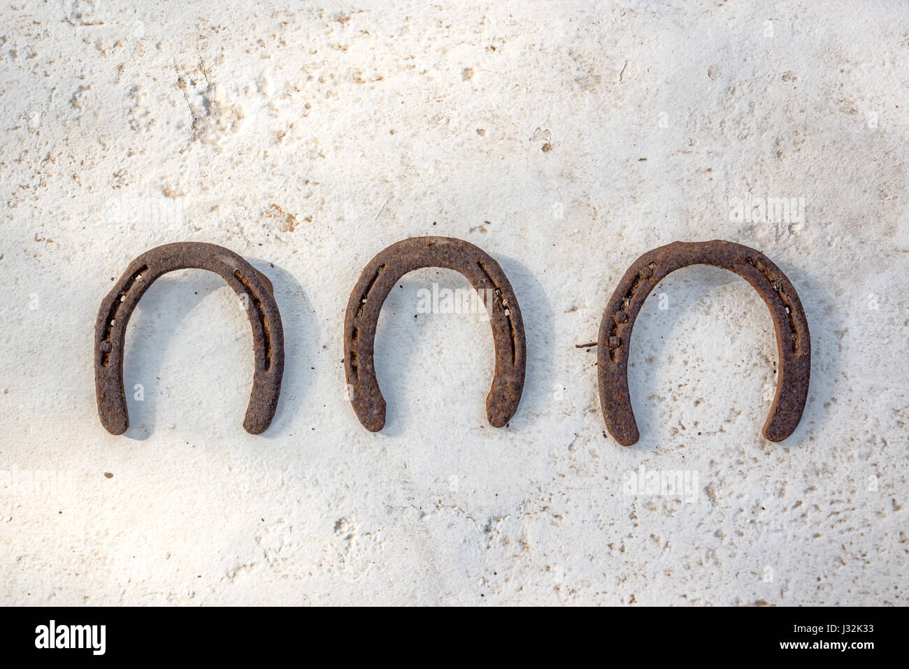 Three old rusty horseshoes hanging on a white wall, luck symbol Stock Photo