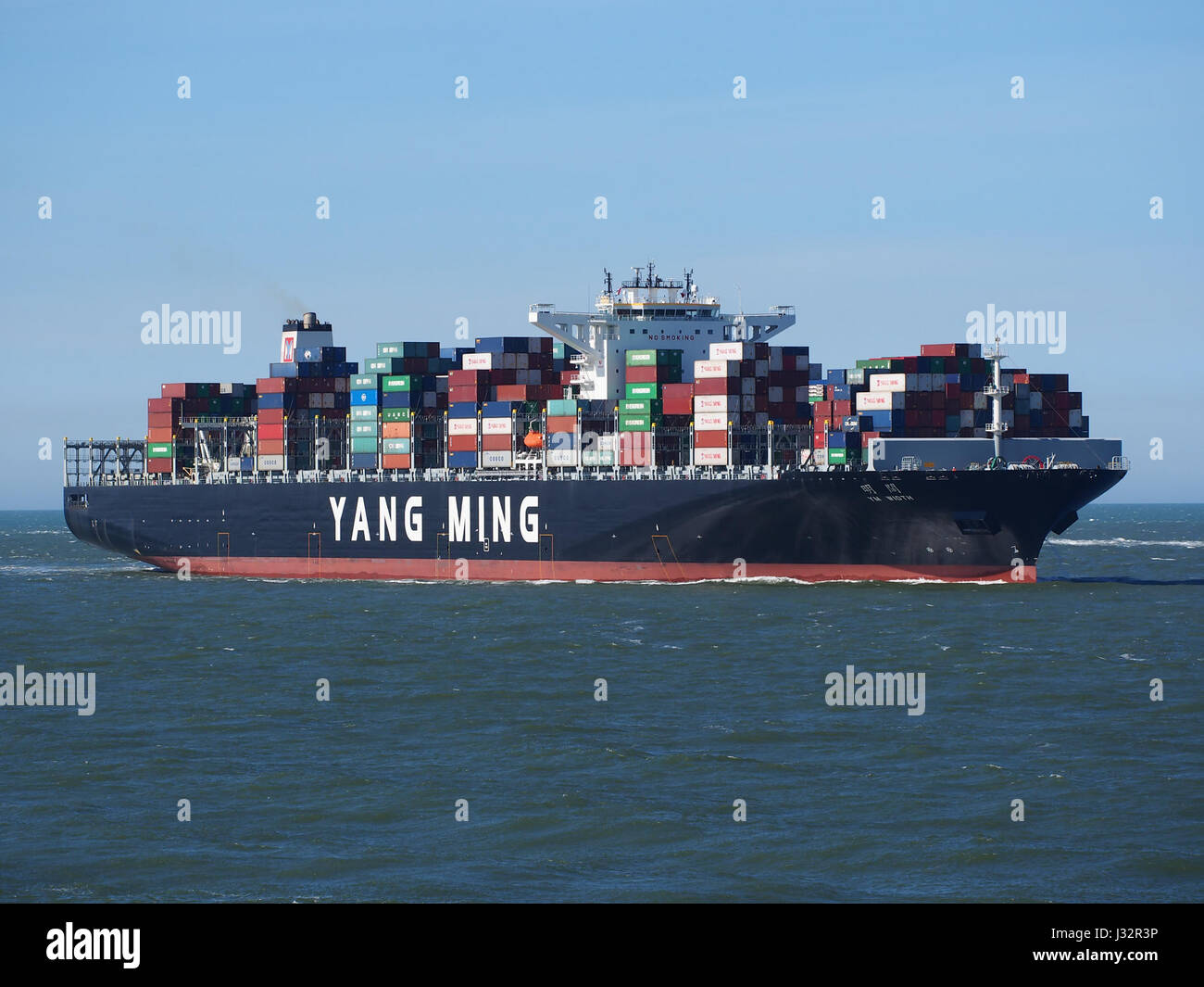 A photograph of the ship YM Width, arriving at the Port of Rotterdam in 2016. The image captures the vessel's large size and portside activity, typical for commercial cargo operations. Stock Photo